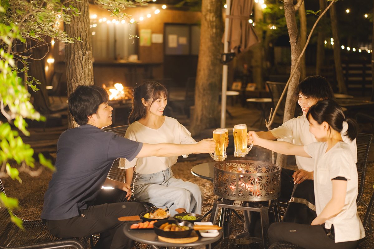 夜の森でBBQを囲んで乾杯する大人たち