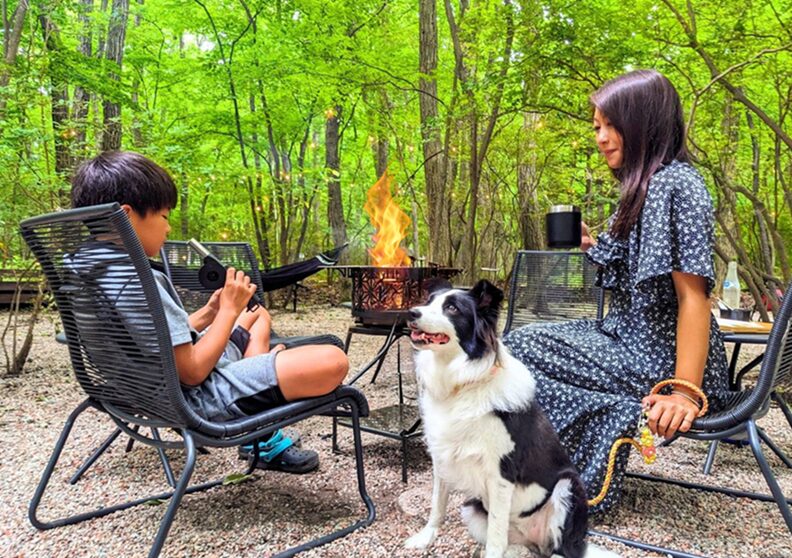 森のたき火のそばで、愛犬とくつろぐ家族